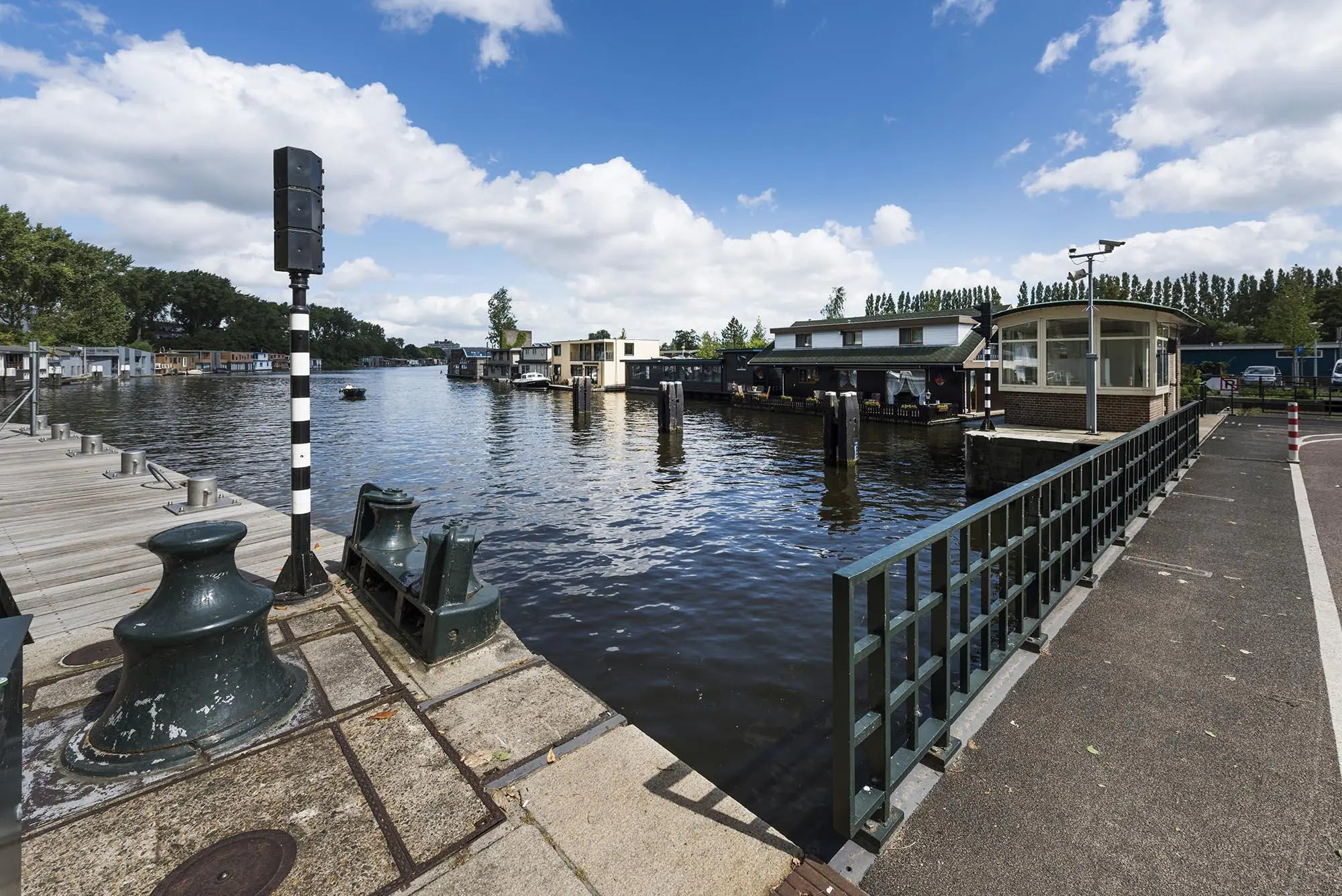 Uitzicht op het water bij de Anthony Fokkerweg met woonboten, een brug en een bedieningshuisje onder een deels bewolkte lucht.